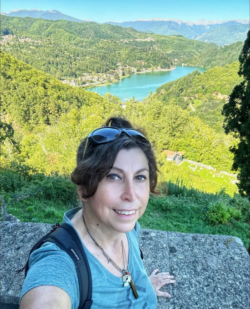 Sabrina, guida e autrice, nel cortile della Chiesa Vecchia di Gorfigliano con vista sul Lago di Gramolazzo