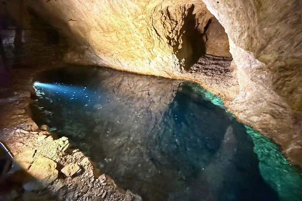 Laghetto sotterraneo nel tunnel con riflessi turchesi illuminato da una lampada